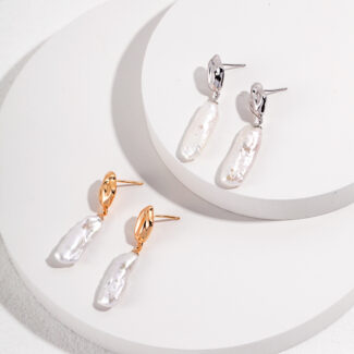 Two pairs of elegant earrings with pendants, one pair set in silver and the other in rose gold, displayed on a white circular stand with a shadowed background. Elegant pearl jewelry