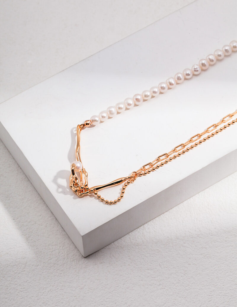 A delicate necklace with a small pendant rests beside a string of natural pearl jewelry on a white display box, showcasing elegance and simplicity in a softly lit setting. Elegant pearl jewelry