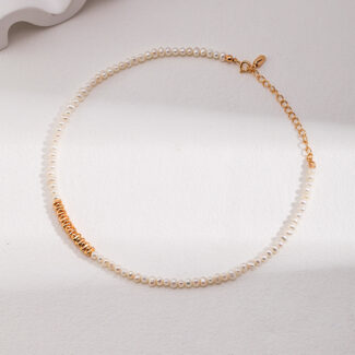 A natural necklace with a gold clasp and small gold detail sits on a white surface under soft lighting, creating gentle shadows. Elegant pearl jewelry