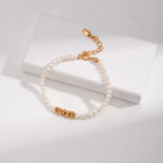 A bracelet with a gold clasp, categorized as gold pearl jewelry, rests on a white rectangular box placed on a light grey textured surface, illuminated by natural light. Elegant pearl jewelry