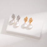 Three pairs of pearl earrings displayed on a white stand, featuring sterling pearl jewelry and gold pearl jewelry designs with large pearl drops, on a textured light background. Elegant pearl jewelry