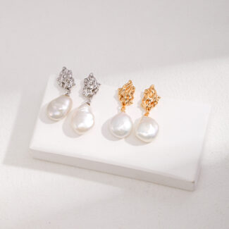 Three pairs of pearl earrings displayed on a white stand, featuring sterling pearl jewelry and gold pearl jewelry designs with large pearl drops, on a textured light background. Elegant pearl jewelry