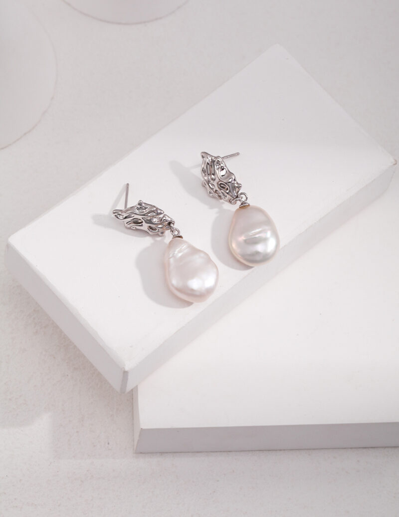 A pair of elegant earrings with intricate sterling details, displayed on a white stand against a soft-textured background. Elegant pearl jewelry