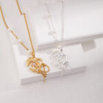 Two necklaces featuring freshwater pearl butterfly pendants, one gold and one silver, displayed on a white stand against a textured background. Elegant pearl jewelry