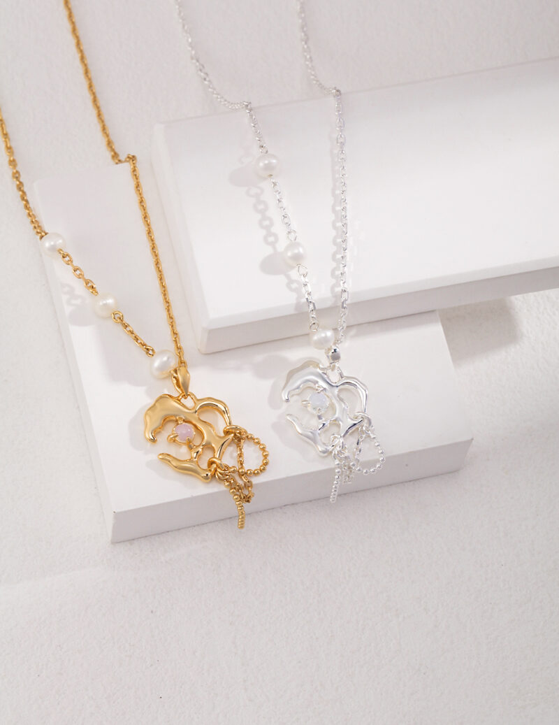 Two necklaces featuring freshwater pearl butterfly pendants, one gold and one silver, displayed on a white stand against a textured background. Elegant pearl jewelry