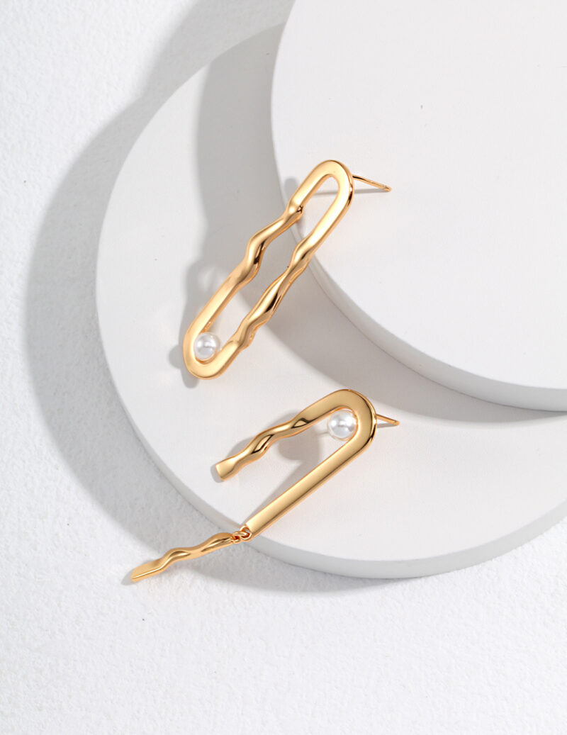 Two elegant gold hairpins from the o_1h5p2upta129ksgnd6p16ni160915 are displayed on round, white platforms. Each hairpin features a sleek, wavy design with a single white pearl accent near one end. The hairpins are artistically arranged to showcase their curves and details. Elegant pearl jewelry