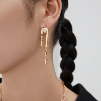 Profile view of a woman wearing unique dangling earring with a pearl accent and a matching gold necklace, against a light background. Her hair is styled in a neat braid Elegant pearl jewelry