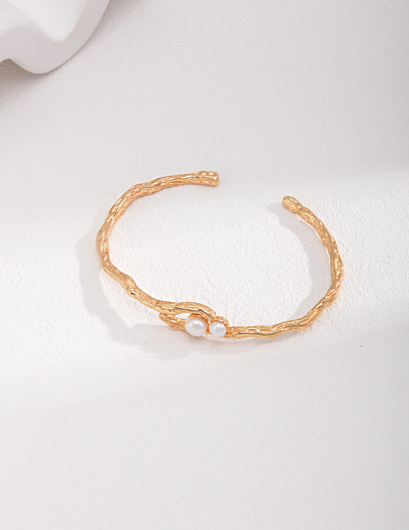 Golden bracelet with a twisted texture and a freshwater pearl set at the center, displayed on a white background. Elegant pearl jewelry