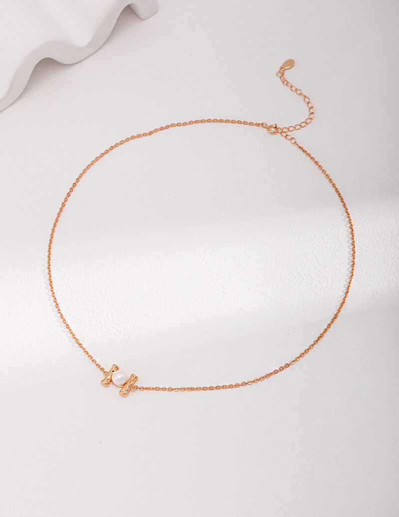 A delicate necklace with a small heart pendant, showcased on a white background, features a fine, linked texture and includes an adjustable clasp enhanced with natural pearl. Elegant pearl jewelry