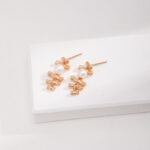 A pair of elegant earrings with natural pearl accents displayed on a white rectangular platform against a light textured background. Elegant pearl jewelry