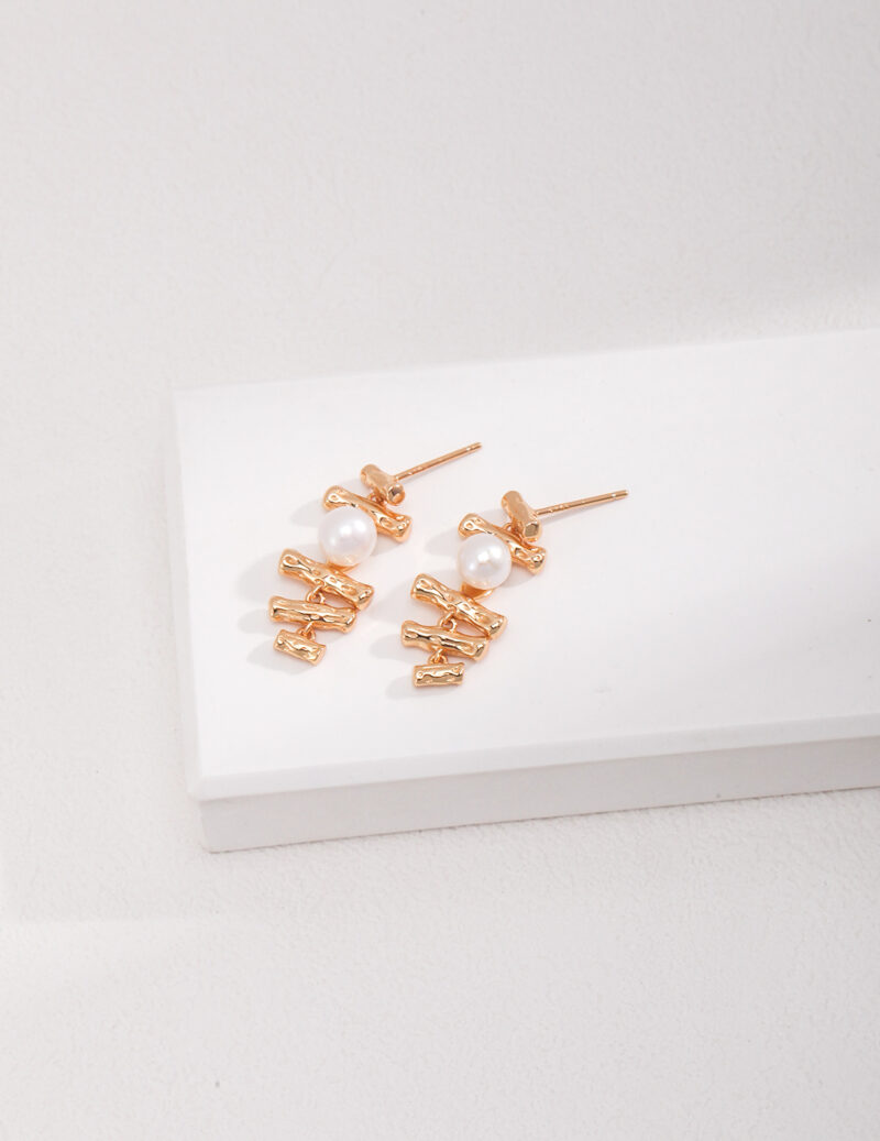 A pair of elegant earrings with natural pearl accents displayed on a white rectangular platform against a light textured background. Elegant pearl jewelry