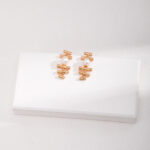 A set of elegant earrings displayed on a white rectangular block against a textured light gray background. Elegant pearl jewelry