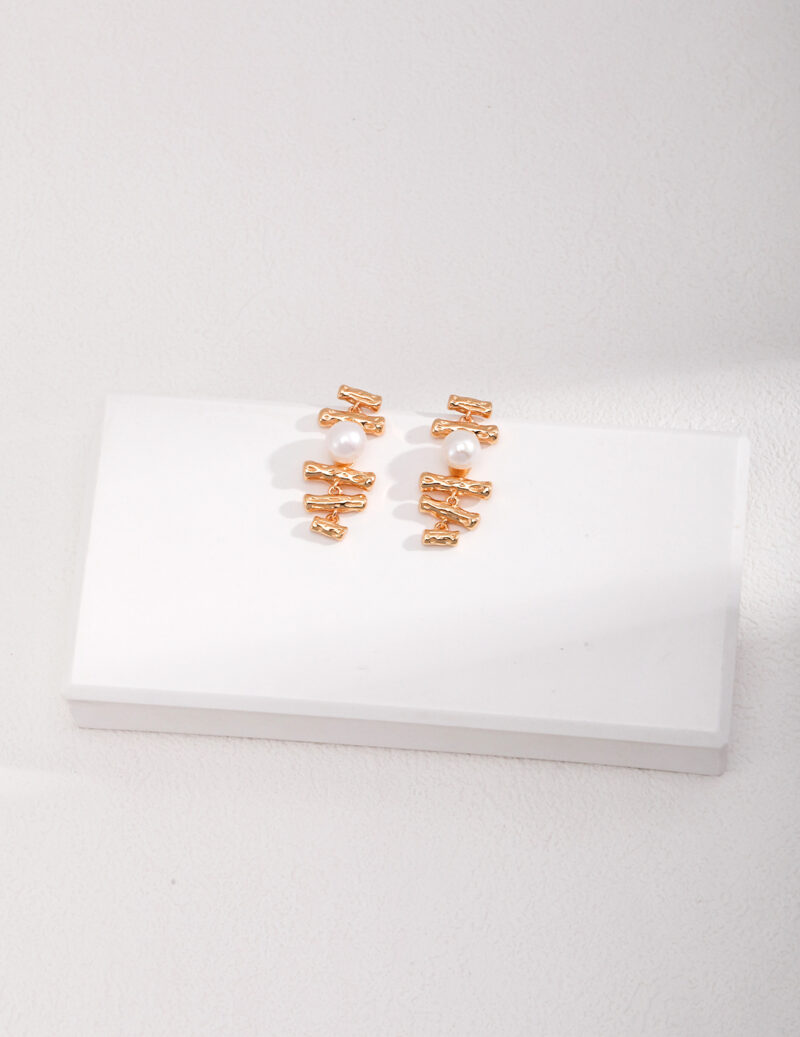 A set of elegant earrings displayed on a white rectangular block against a textured light gray background. Elegant pearl jewelry