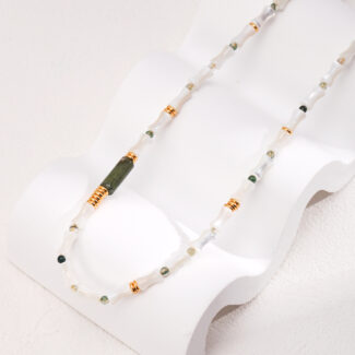 A delicate necklace with green and clear beads, highlighted by stone accents, draped gracefully on a white, wave-shaped jewelry stand against a cream background. Elegant pearl jewelry