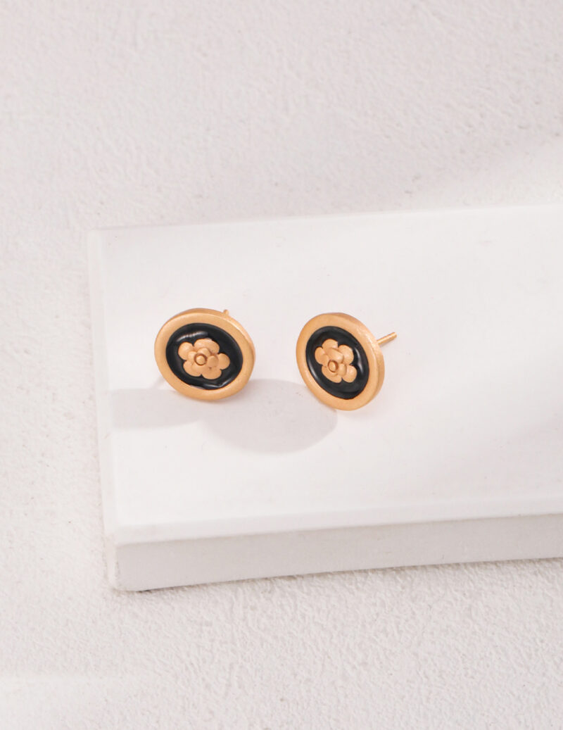 A pair of earrings with a floral design in the center, featuring freshwater pearls, displayed on a white rectangular surface against a textured white wall. Elegant pearl jewelry