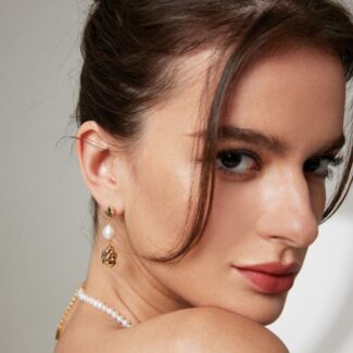 Close-up portrait of a woman with a bun hairstyle, wearing drop earrings and a pearl necklace, looking over her shoulder with a soft gaze. Elegant pearl jewelry