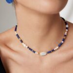 Sentence with product name: Close-up of a woman wearing a necklace featuring a central natural pearl pendant, paired with a matching blue earring. Elegant pearl jewelry