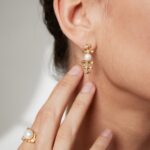 Close-up view of a woman's ear wearing an elegant earring, with her hand showcasing a matching ring. Her smooth skin and refined jewelry highlight a sophisticated style. Elegant pearl jewelry