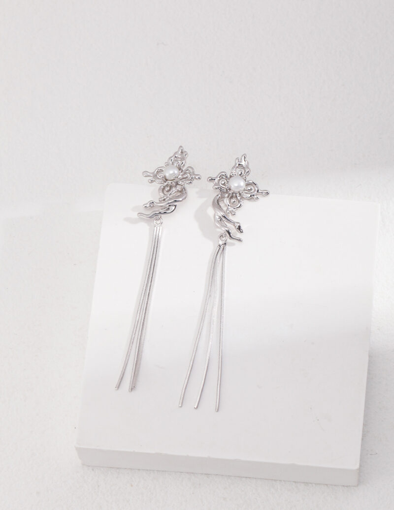 Elegant earrings with floral motifs at the top and long, dangling tassel-like strands featuring natural pearl, displayed against a white background. Elegant pearl jewelry