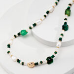 A necklace with alternating green stones and freshwater pearls on a white display stand, featuring a gold clasp and accents. Elegant pearl jewelry