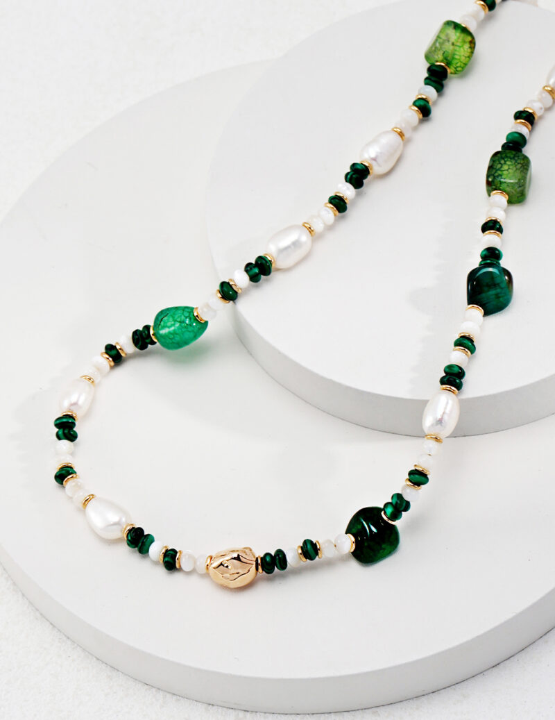 A necklace with alternating green stones and freshwater pearls on a white display stand, featuring a gold clasp and accents. Elegant pearl jewelry