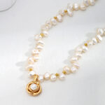 A necklace with natural pearl and a golden pendant shaped like a rose, lying on a light surface. Elegant pearl jewelry