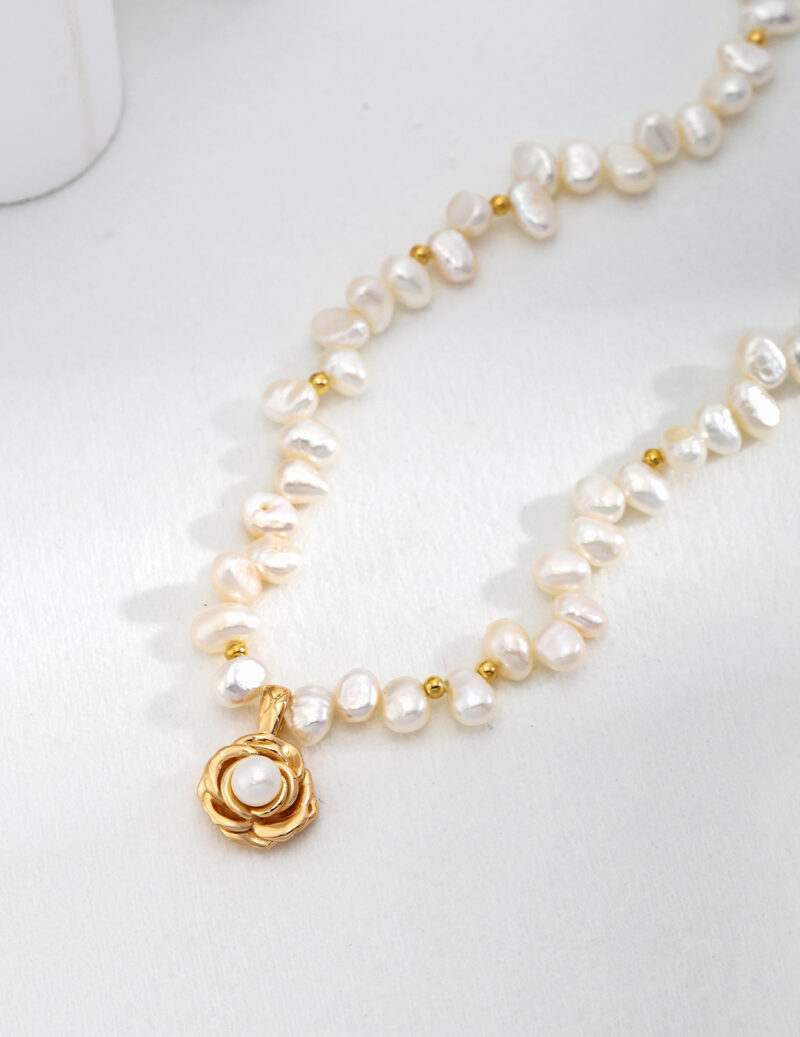 A necklace with natural pearl and a golden pendant shaped like a rose, lying on a light surface. Elegant pearl jewelry