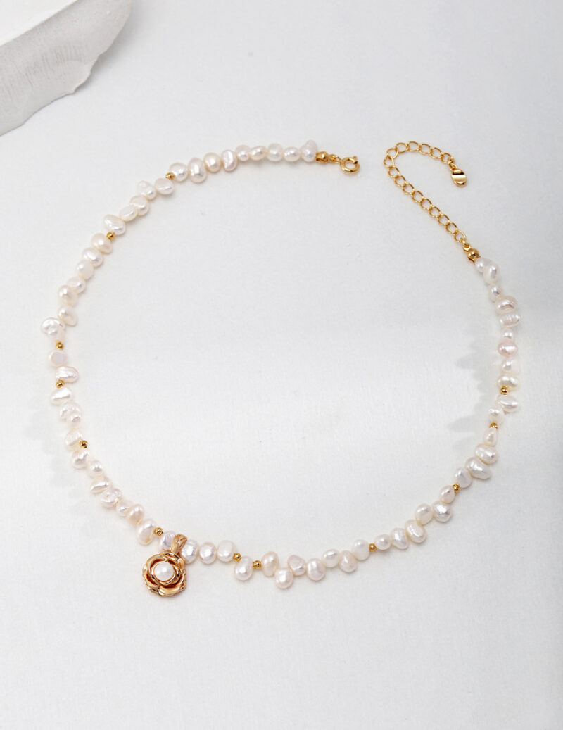 A necklace with a gold clasp laid flat on a light gray surface, featuring irregularly shaped pearls interspersed with small gold beads. Elegant pearl jewelry