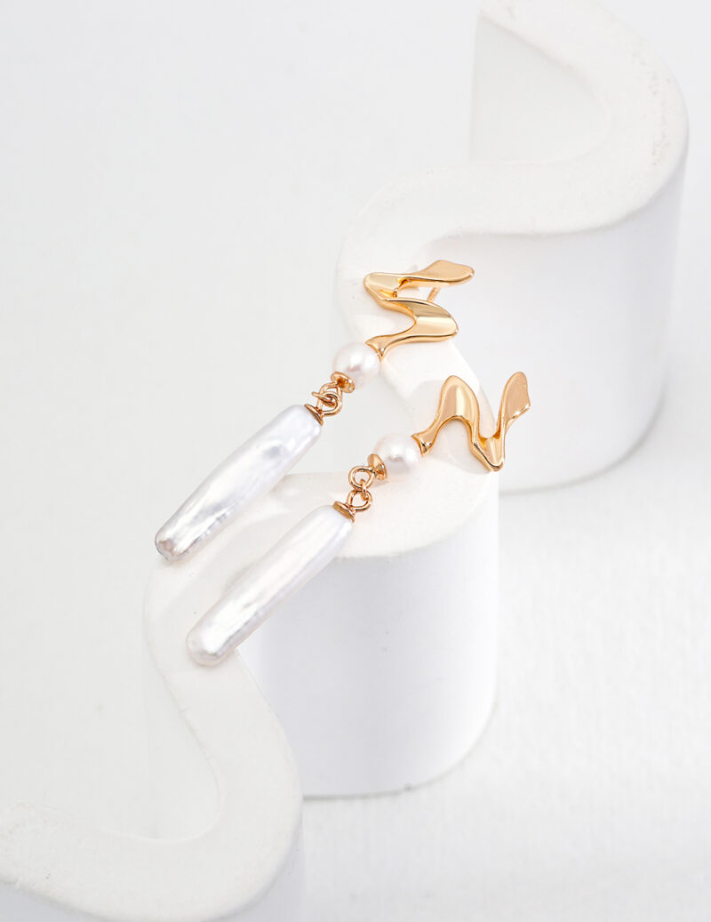 Three elegant earring displayed on a clear, wavy glass holder against a white backdrop. Two earrings have abstract wave designs and one is a simple hoop, all featuring natural pearl accents. Elegant pearl jewelry