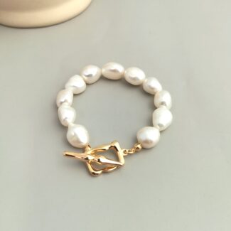 A o_1fi97o44bgm2a831t295ck10gqt bracelet with irregularly shaped white pearls and a gold clasp, displayed on a soft beige background. Elegant pearl jewelry