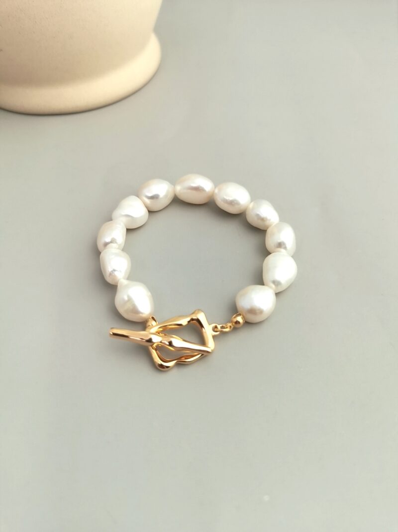 A o_1fi97o44bgm2a831t295ck10gqt bracelet with irregularly shaped white pearls and a gold clasp, displayed on a soft beige background. Elegant pearl jewelry