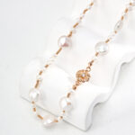 Elegant o_1hsn3fdmekqv1v3p153h1vnq1qr4 with gold vermeil accents and floral pendant displayed on a white stand against a plain background. Elegant pearl jewelry