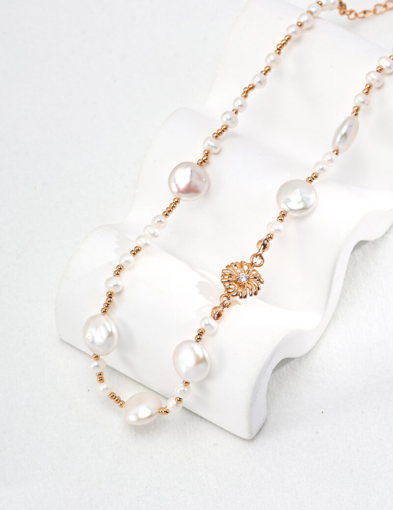 Elegant o_1hsn3fdmekqv1v3p153h1vnq1qr4 with gold vermeil accents and floral pendant displayed on a white stand against a plain background. Elegant pearl jewelry