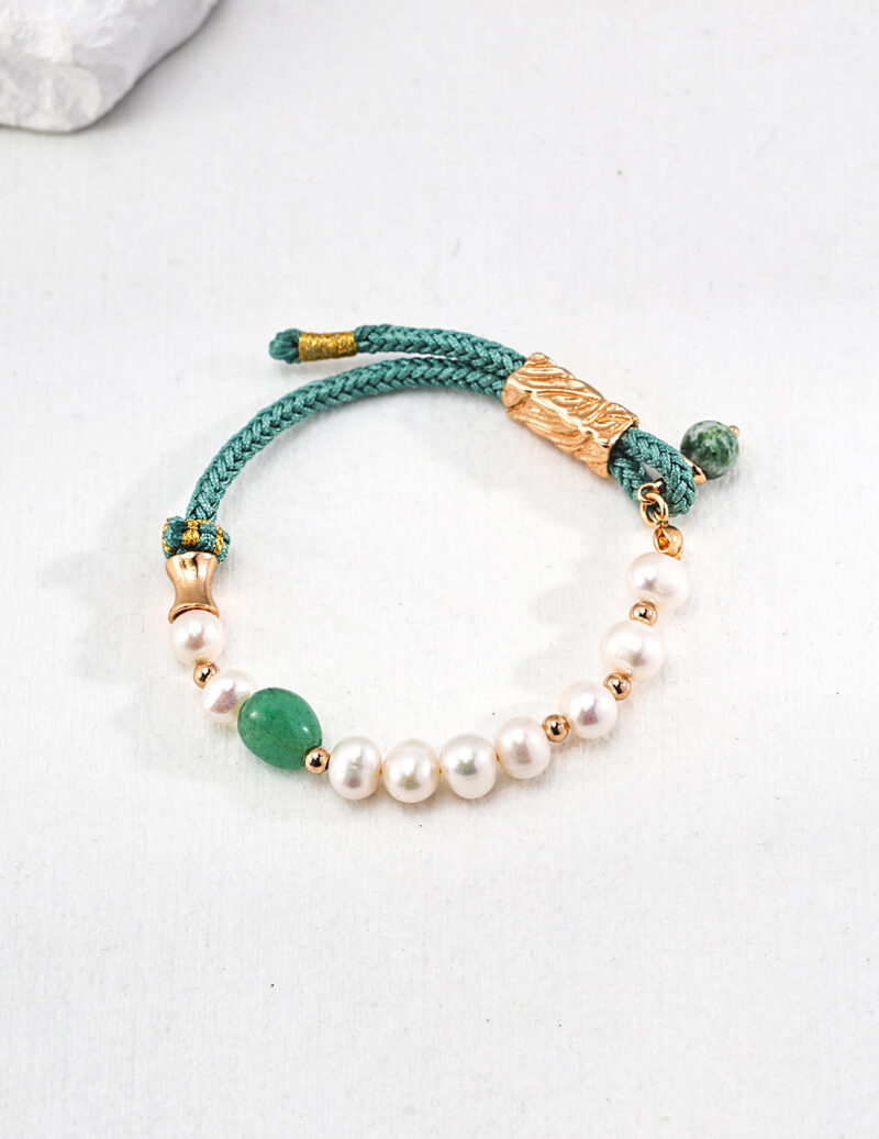 A o_1ht8oi7te1eae1a8n1va41p6a12ef2 adorned with pearls, gold vermeil beads, and green stones on a white surface. A gold clasp shaped like a leaf adds a decorative touch. Elegant pearl jewelry