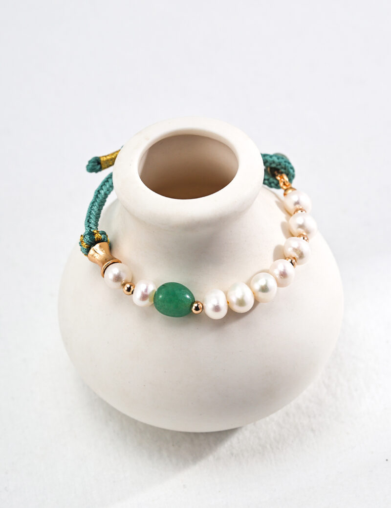 A pearl bracelet with a large o_1ht8oi7terjq8a141e1a3u2ar3 stone and gold vermeil accents displayed on a small white ceramic mannequin neck stand against a light background. Elegant pearl jewelry