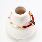 An elegant o_1htdsofdf13qrmut3jk1e116nk8 with a combination of red threads, pearls, and gold vermeil links displayed on a small white ceramic jewelry holder. Elegant pearl jewelry