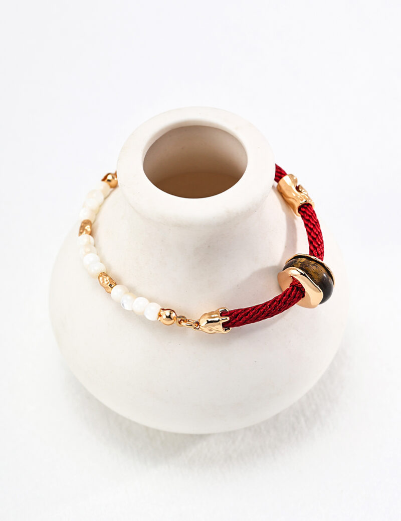 An elegant o_1htdsofdf13qrmut3jk1e116nk8 with a combination of red threads, pearls, and gold vermeil links displayed on a small white ceramic jewelry holder. Elegant pearl jewelry