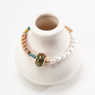 A colorful braided and pearl necklace with a large, green [product:o_1htdt5tu0u0114a9j67rcf601] clasp displayed on a white necklace stand. Elegant pearl jewelry