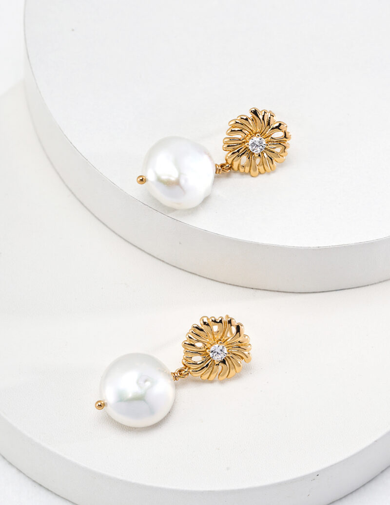 Two elegant earrings rest on white circular platforms. Each earring, part of the Floral Series, features an 18k Gold Vermeil flower-shaped design with a small central gemstone and a large white pearl dangling below. The image showcases the intricate details and luxurious appearance of these o_1htim9ik31aie1092tia3qeghi3. Elegant pearl jewelry