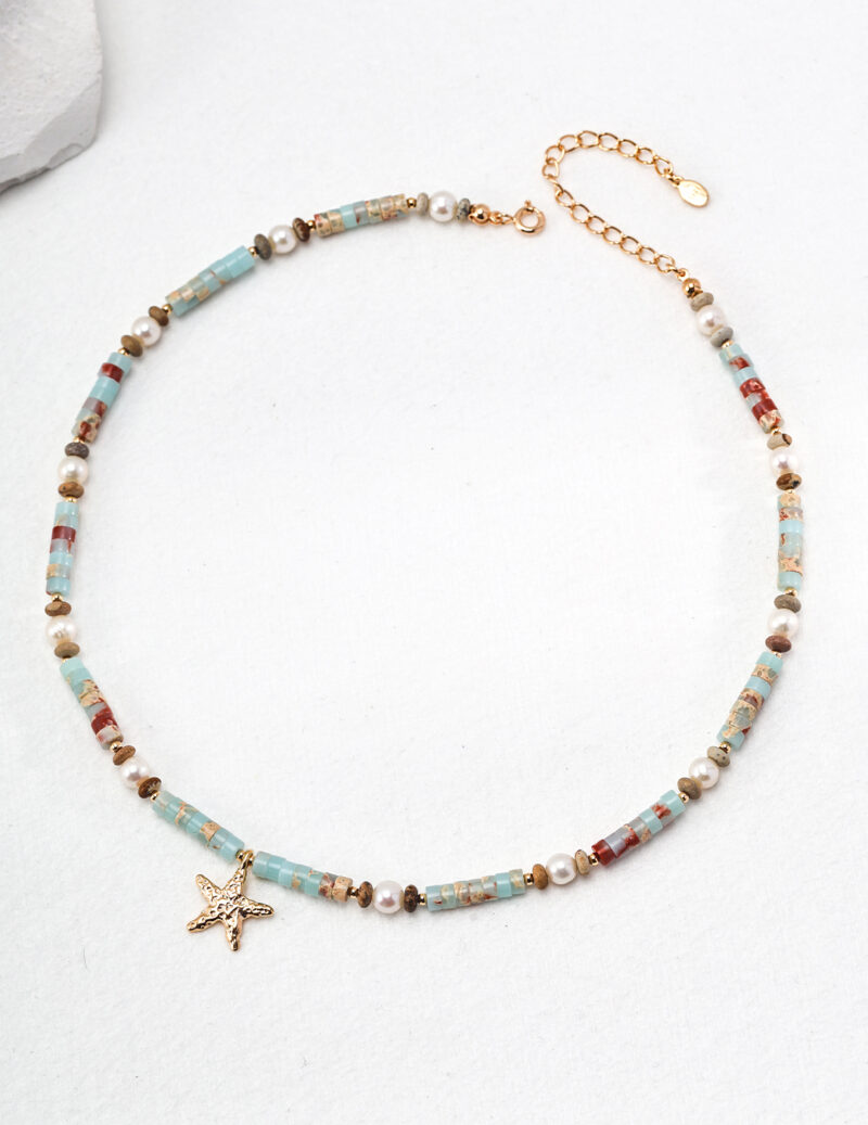 A delicate o_1hucrll2b1fmq1m481lvu11fe10e6b with a chain of small beads in shades of blue, red, and gold, interspersed with tiny white pearls. A starfish-shaped gold charm dangles from the center, making it perfect for summer fun. The necklace has an adjustable gold clasp. Elegant pearl jewelry