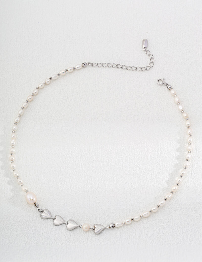 A delicate necklace featuring small white pearls and five heart-shaped silver charms at the center, with an adjustable silver chain and clasp. The o_1hv8s3jhq13dh1h6qmiv4n717bl0 is displayed against a white background. Elegant pearl jewelry