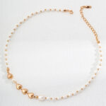 A delicate o_1hv8s3jhrkjha2o1gqs1hku1rsm3 with small gold heart accents is laid out on a white surface. The necklace features an adjustable gold chain clasp and is adorned with evenly spaced pearls and heart-shaped gold pieces for an elegant, minimalist design. Elegant pearl jewelry