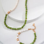 The o_1i0aipujb1uqt15knrlm1m7u127i0 jewelry set features a necklace and bracelet elegantly arranged on a white circular display. The necklace showcases beautiful segments of green beads paired with a single strand of lustrous white pearls. The bracelet artistically alternates green beads with small white pearls, all accented by 18k Gold Vermeil fittings and secured with a gold clasp. Elegant pearl jewelry