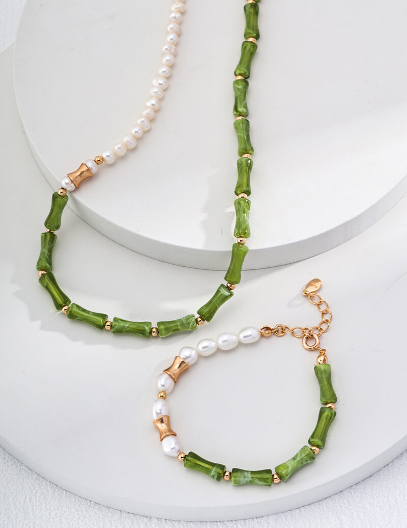 The o_1i0aipujb1uqt15knrlm1m7u127i0 jewelry set features a necklace and bracelet elegantly arranged on a white circular display. The necklace showcases beautiful segments of green beads paired with a single strand of lustrous white pearls. The bracelet artistically alternates green beads with small white pearls, all accented by 18k Gold Vermeil fittings and secured with a gold clasp. Elegant pearl jewelry