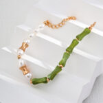 A beaded bracelet featuring alternating white pearls and green jade-like cylindrical beads, separated by elegant 18k gold vermeil spacer beads. The bracelet is displayed on a white, stepped surface. The clasp is a gold lobster claw with an adjustable chain. Product Name: o_1i0aipujc14ukc1lq41qosq482 Elegant pearl jewelry