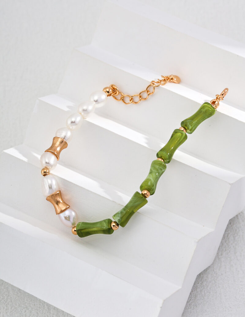 A beaded bracelet featuring alternating white pearls and green jade-like cylindrical beads, separated by elegant 18k gold vermeil spacer beads. The bracelet is displayed on a white, stepped surface. The clasp is a gold lobster claw with an adjustable chain. Product Name: o_1i0aipujc14ukc1lq41qosq482 Elegant pearl jewelry