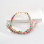 A colorful braided friendship bracelet with a mix of pastel threads and small tassels on each end, adorned with five white beads in the center, displayed on a white background. Exuding rustic elegance, the o_1i0d4pcs51nup1uluo5fvoj1of95 rests on a rectangular white platform beneath part of the bracelet. Elegant pearl jewelry