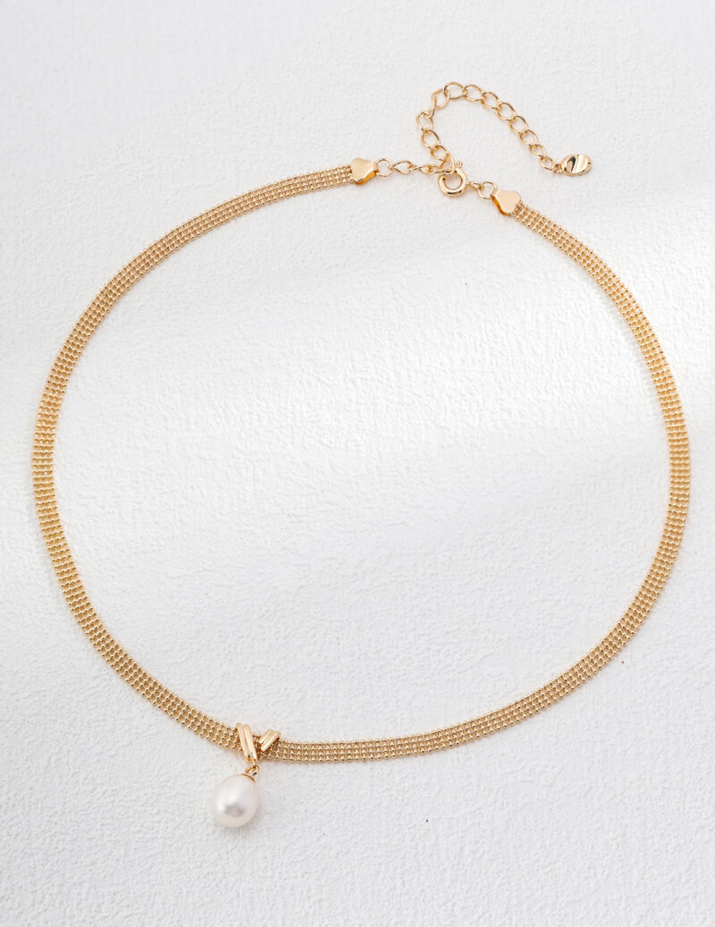 The o_1i0fcngqb18od11fajg11r9ap3s3 features a delicate gold choker necklace with a small, white pearl pendant. This 18k gold vermeil piece features a fine chain design and an adjustable clasp with an extension chain. The pearl is suspended from a small, geometric gold setting at the center, resembling elegant lace patterns. Elegant pearl jewelry