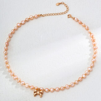 The o_1ia1s7qhr11ld1e0ett91jgemk52, a delicate pearl necklace with small pink pearls beautifully linked together, is accented by a gold vermeil butterfly charm. Displayed in a circular arrangement on a light, textured background, this elegant piece embodies the grace of a perfectly tied bowtie. Elegant pearl jewelry