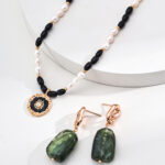 Explore the o_1iac7l2s8gdt10gtrmf1f20196r3, a minimalist jewelry set consisting of a necklace decked with black and white beads, complemented by a gold and black sunburst-patterned pendant, along with matching gold earrings featuring rectangular green stones. The faux amber tones beautifully enhance the display's white background, adding warmth to your style. Elegant pearl jewelry